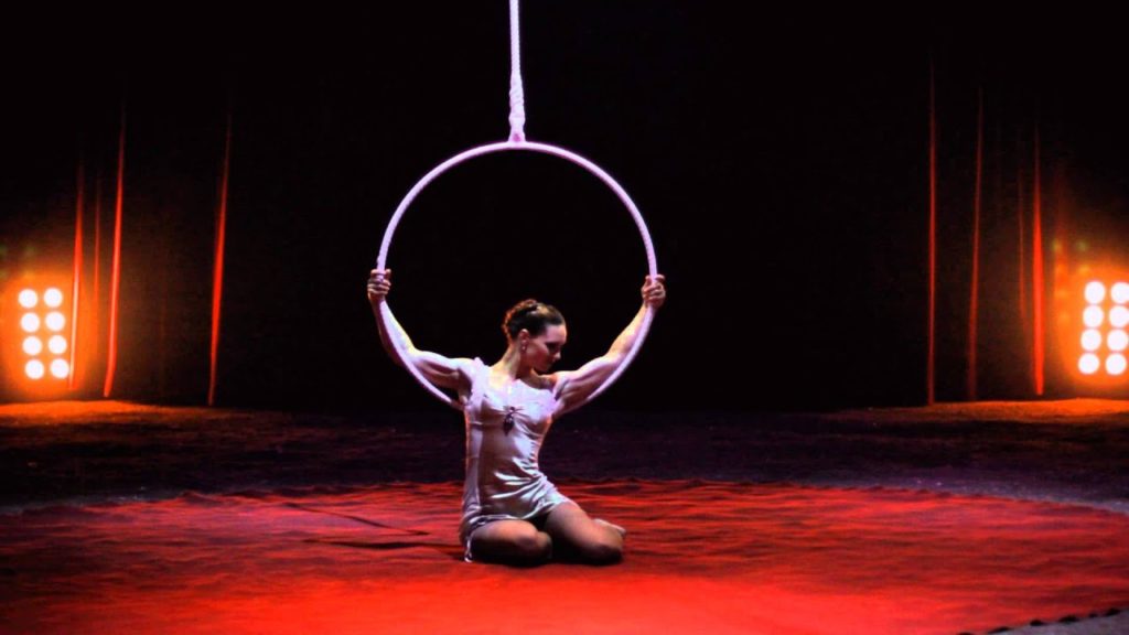A photo of aerialist Chloe Gardiol sitting on the ground, holding her hoop above her head.