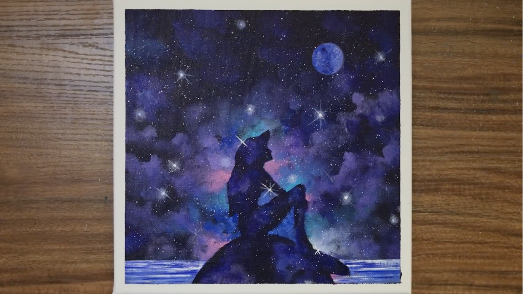 A photo of the finished painting by Serena Art of the Little Mermaid. Ariel is sitting on a rock in the ocean, in silhouette, looking up at the night sky.