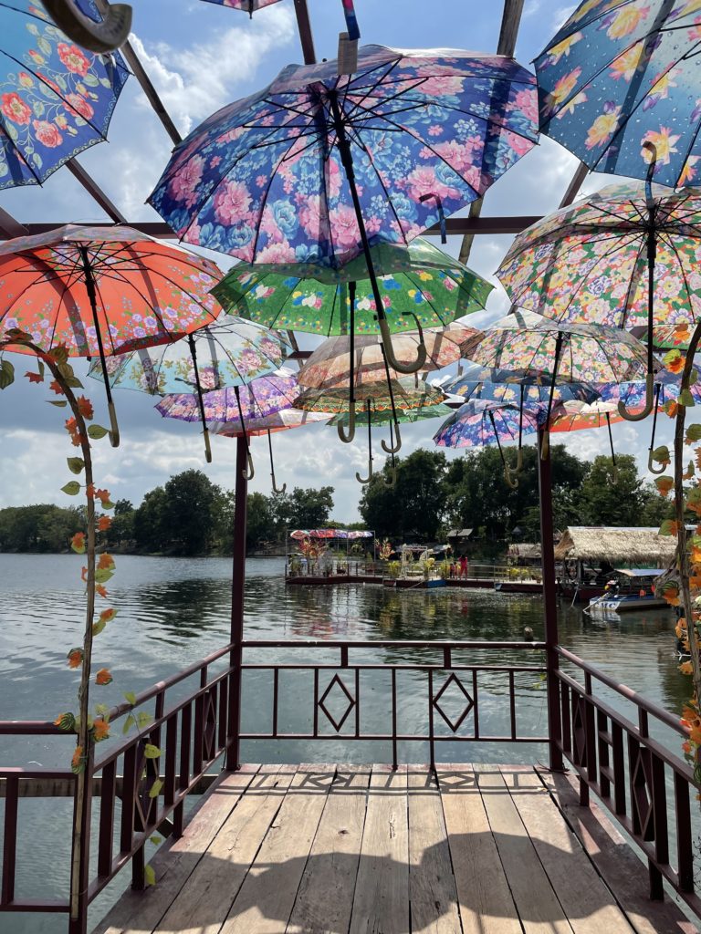 A photo of a dock on a lake in Cambodia. There is an archway of brightly coloured umbrellas overhead.