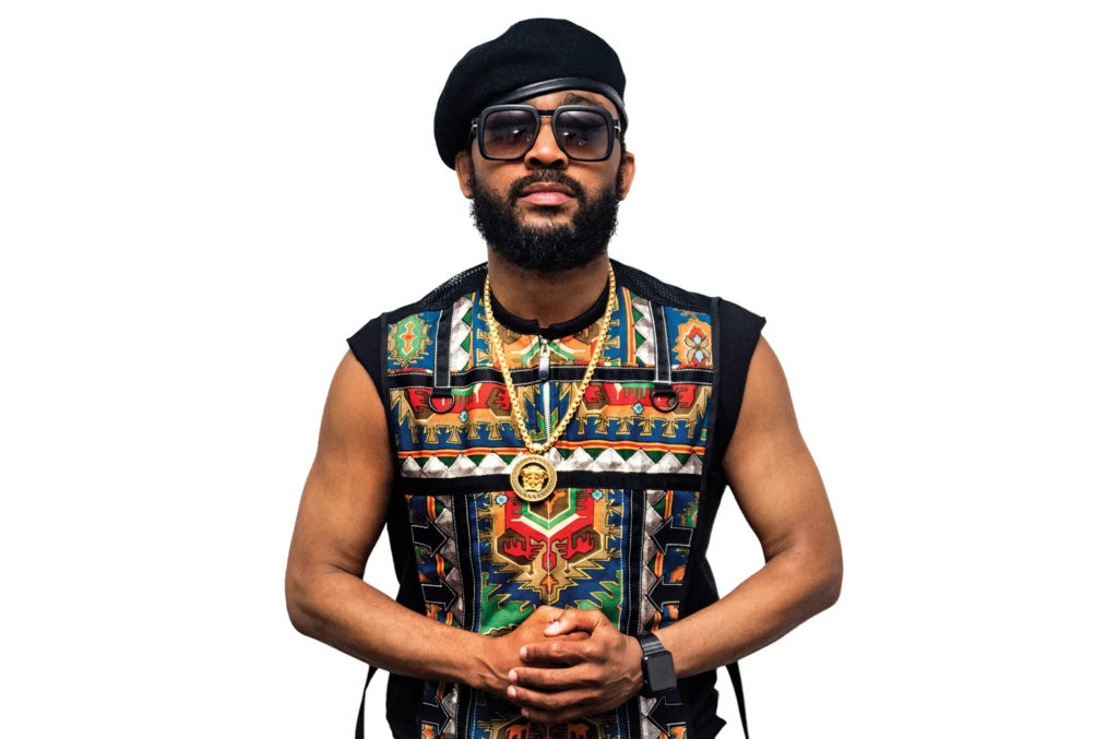 A photo of Machel Montano. It is taken from the waist up, and he is posing directly into the camera in front of a blank white background.